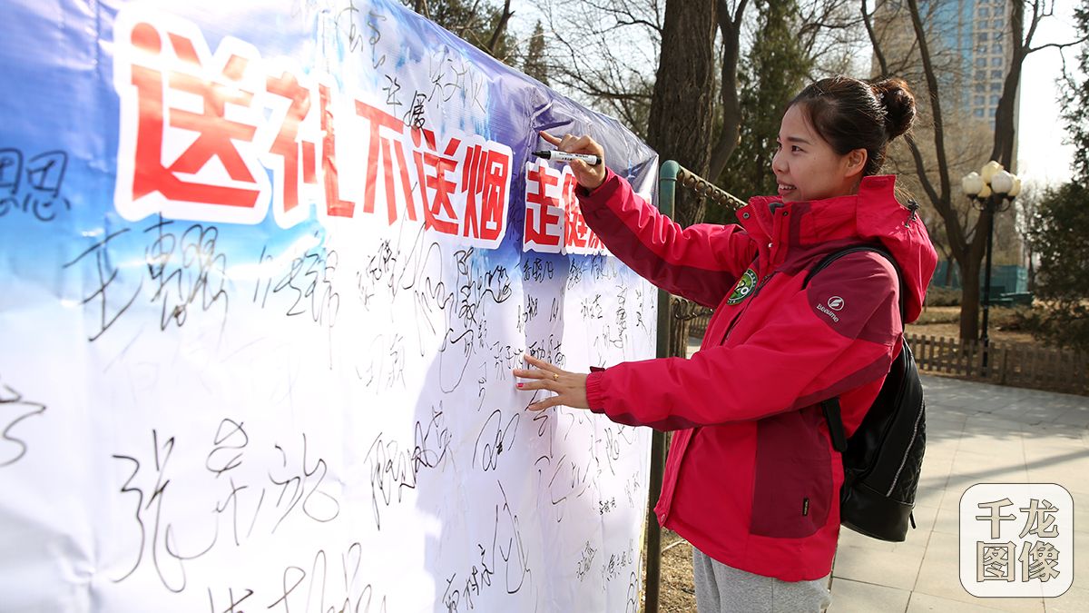 2月22日，丰台区卫计委及丰台疾控中心开展“春节送礼不送烟，健健康康过大年”活动。图为社区居民在“送礼不送烟”的背板上签字。千龙网记者 王悦摄